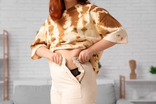 Image of woman trying to do her trousers up after pregnancy weight gain Crewe