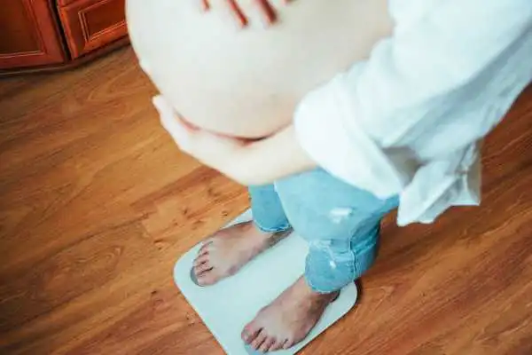 Image of woman weighing herself and experiencing weight gain through pregnancy Crewe