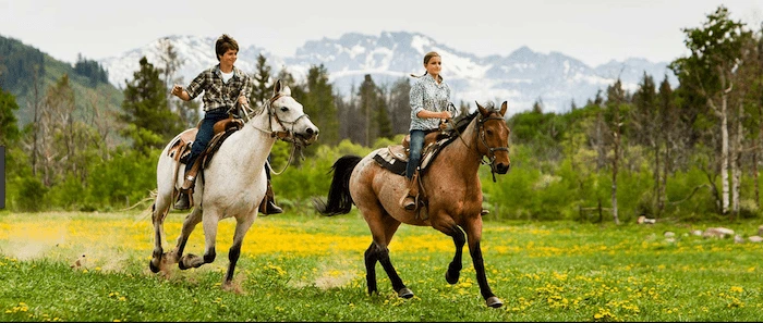 Confident plus-size woman riding Crewe a horse through a field with a smile on her face.